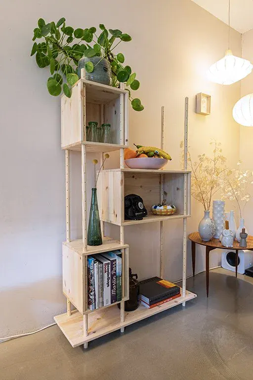 A narrow RMC in a corner of a room, with a trailing plant on top, green bottles and a stack of books